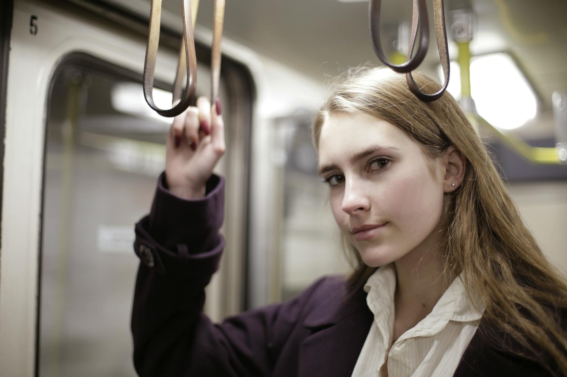 Młoda kobieta w metrze trzyma poręcz i patrzy prosto w obiektyw