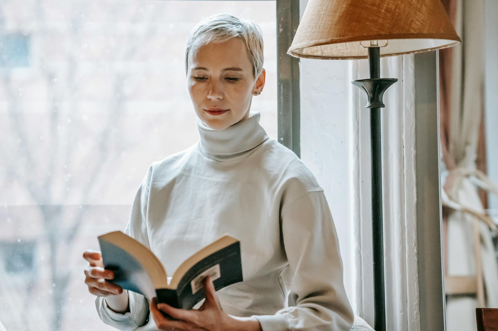 Kobieta o krótkich włosach czyta książkę przy lampie w dziennym świetle