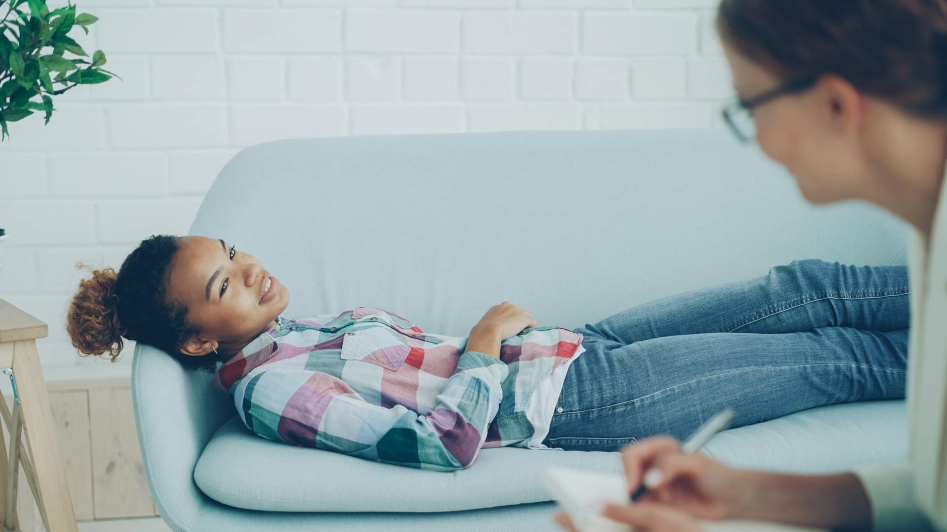 Uśmiechnięta kobieta na terapii leży na kanapie, terapeuta robi notatki