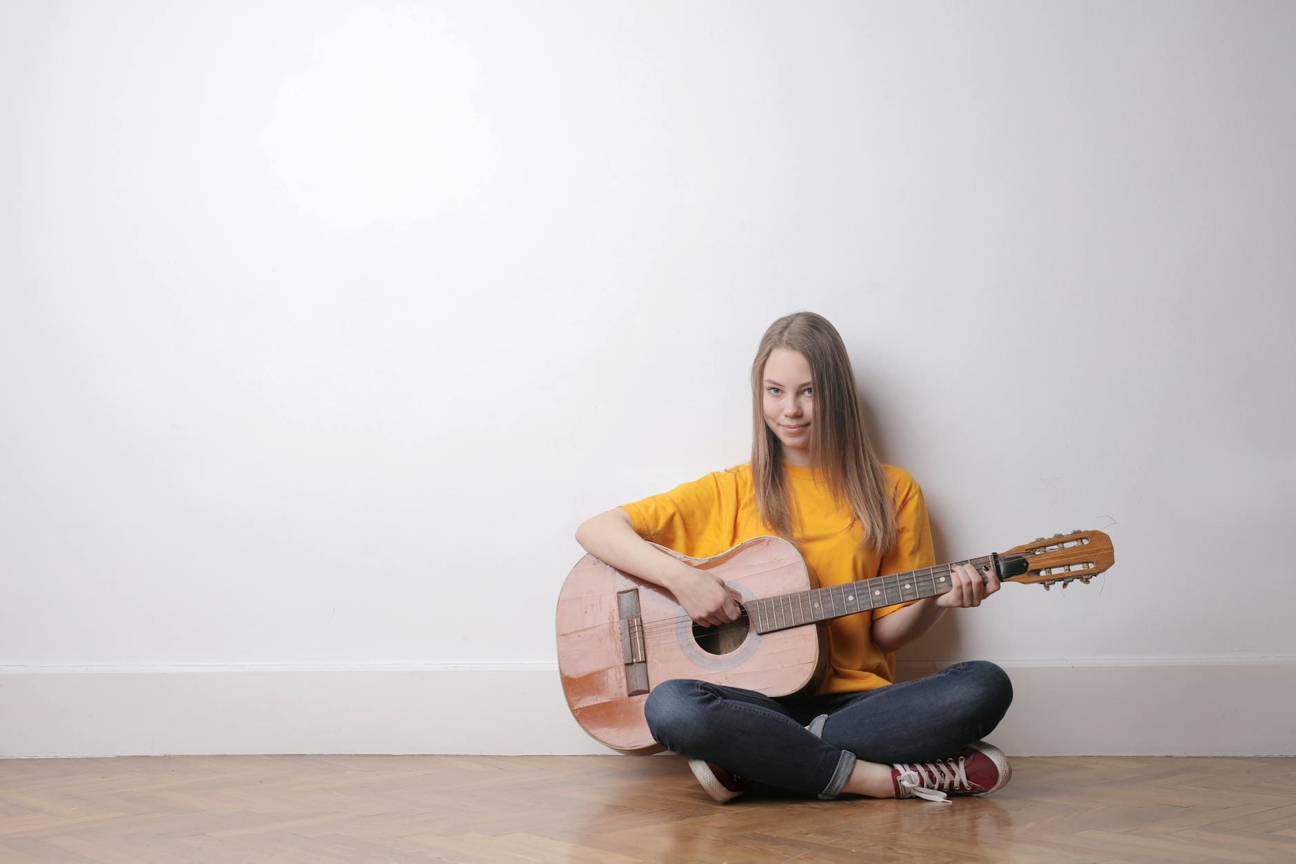 Jak skutecznie uczyć się słówek z piosenek po angielsku: praktyczny przewodnik dla początkujących Młoda kobieta grająca na gitarze akustycznej na tle białej ściany